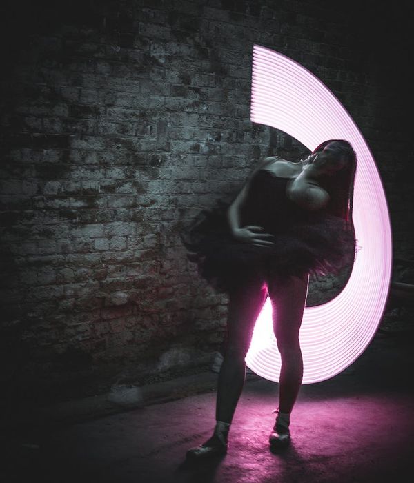 Woman in a dynamic yoga pose against a dark background with pink light trails.